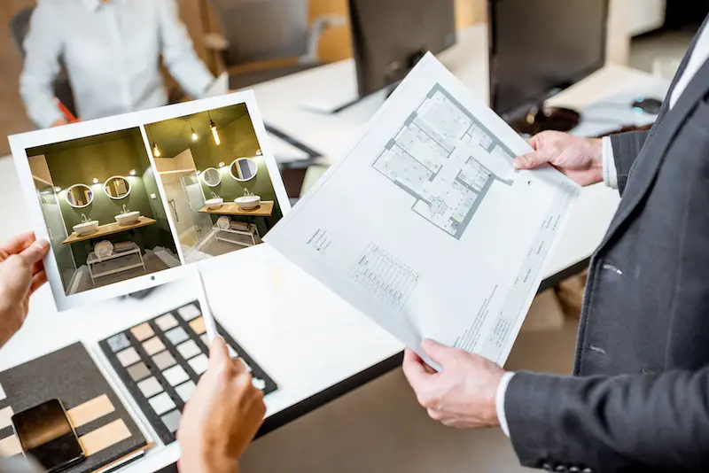 Creative office employees working on some architectural project, holding plans and interior renderings, close-up on the blueprints